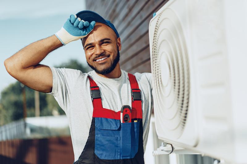 Roo-D's technician smiling beside an outdoor air conditioning unit he just serviced