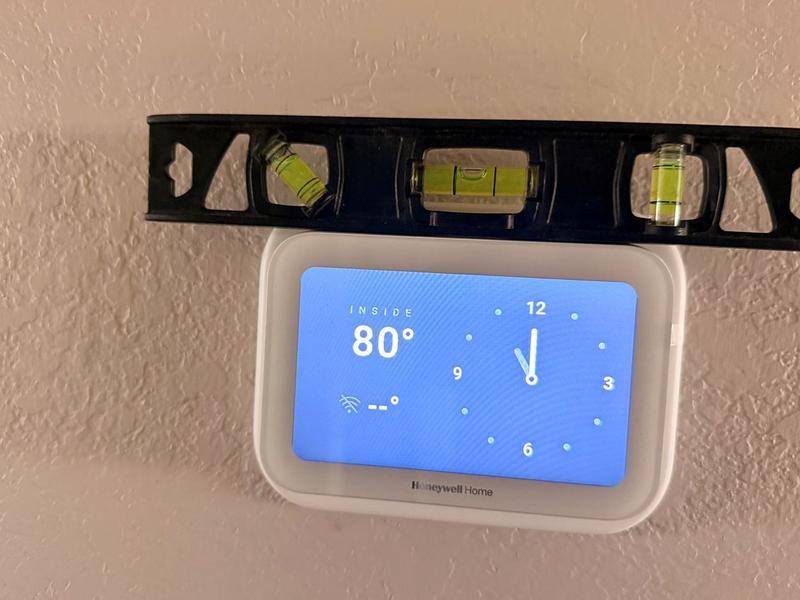 Close-up of a Honeywell Home thermostat being leveled during installation, reading 80 degrees inside
