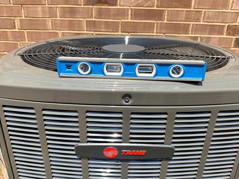 Close-up of a Trane outdoor condenser with a blue level resting on top to confirm it sits level